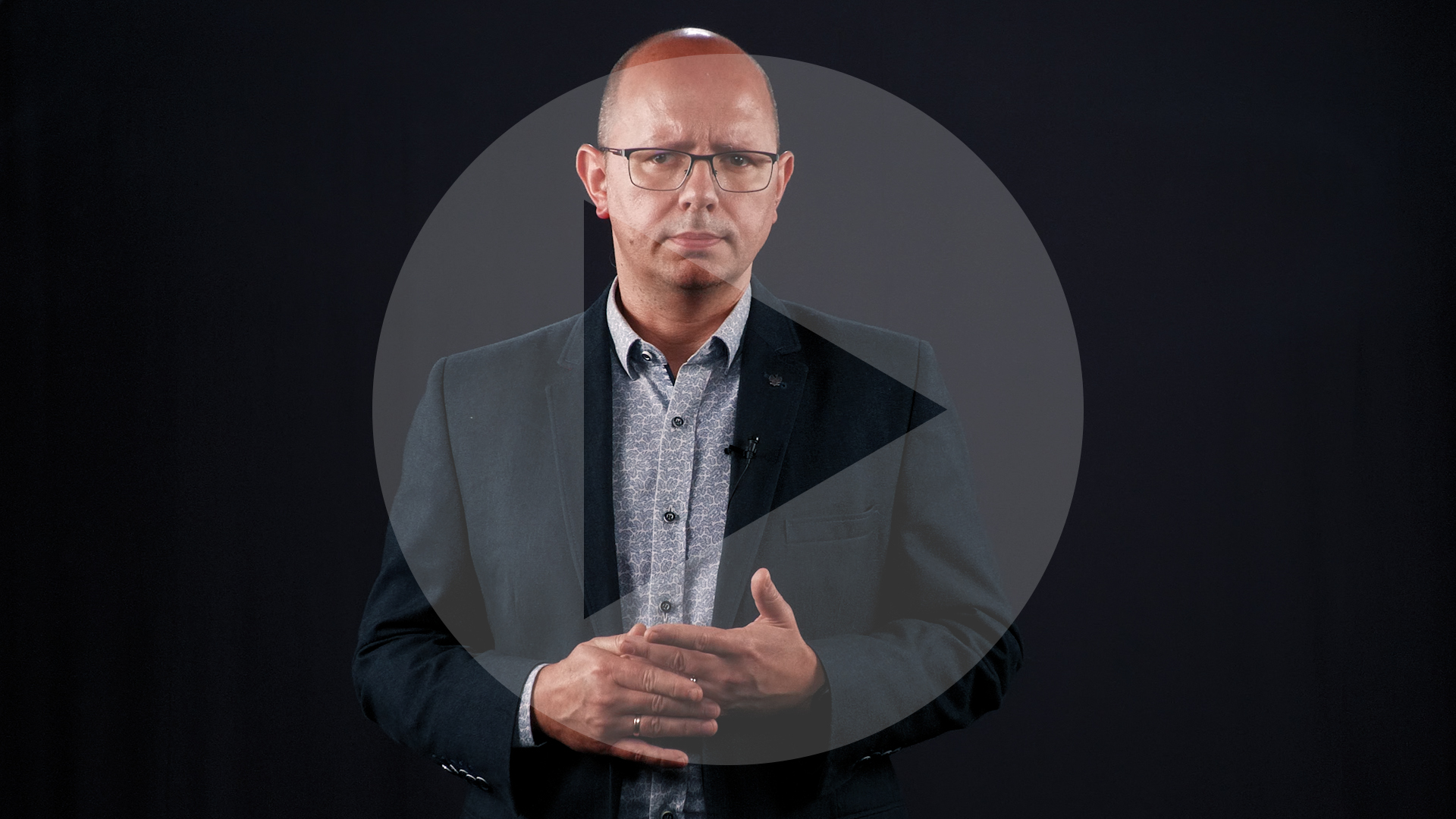 Kadr z nagrania przedstawiający Błażeja Kmieciaka. Na kadr naniesiony jest symbol odtwarzania wideo - trójkąt w kole