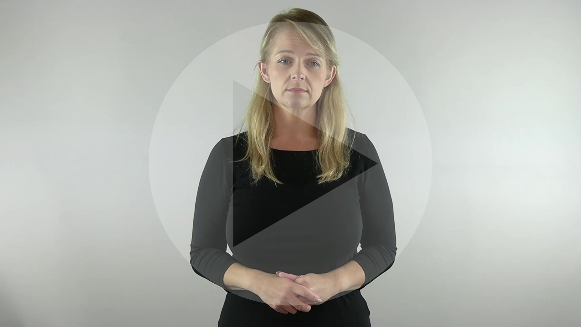 Kadr z nagrania przedstawiający tłumaczkę języka migowego. Na kadr naniesiony jest symbol odtwarzania wideo - trójkąt w kole