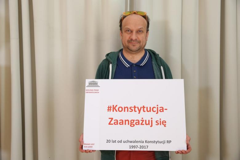 zdjęcie: mężczyznza stoi i trzma planszę z napisem: Konstytucja - zaangażuj się