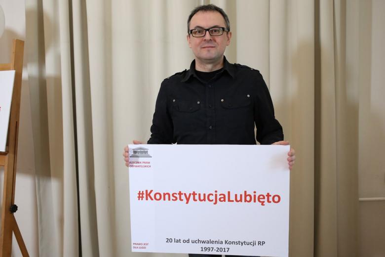 zdjęcie: mężczyzna stoi i trzyma planszę z napisem: Konstytucja lubię to