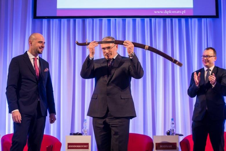 zdjęcie: na scenie stoi trzch mężczyzn, mężczyzna w środku unosi szablę