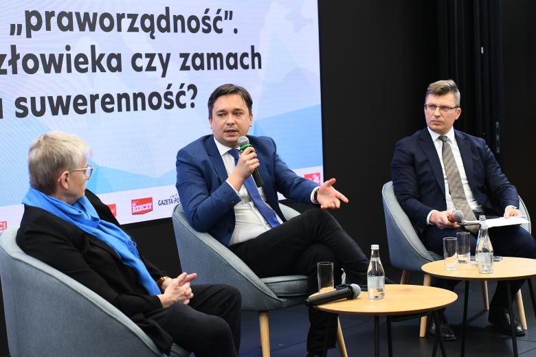 kobieta i 2 mężczyzn siedzi w fotelach i bierze udział w panelu