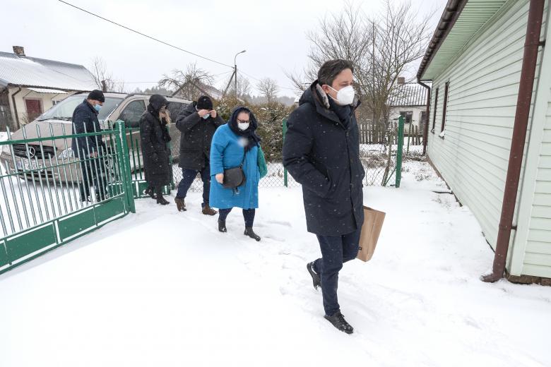 Grupa osób z artykułami pierwszej potrzeby wchodząca przez bramę na wiejskie podwórko