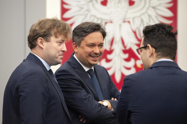 RPO Marcin Wiącek i ZRPO Maciej Taborowski rozmawiający z uczestnikiem konferencji na tle godła Polski