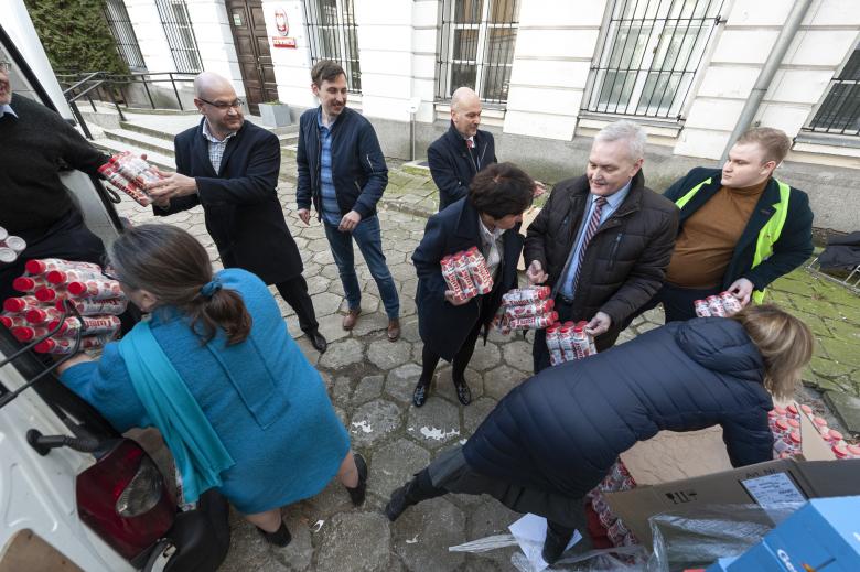 Pracownicy BRPO oraz wolontariusze ustawieni w łańcuszek ładują produkty do bagażnika samochodu.