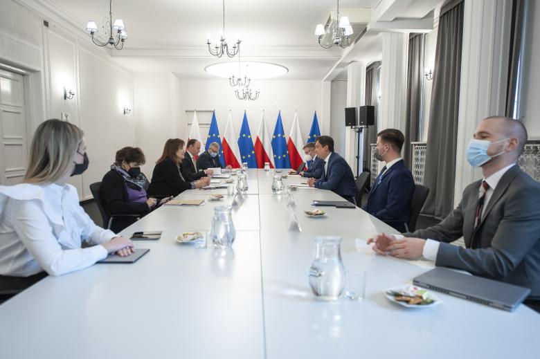 Delegacje RPO i Komisji Europejskiej, siedząc naprzeciwko siebie, rozmawiają przy długim stole konferencyjnym. W tle flagi Polski i Unii Europejskiej