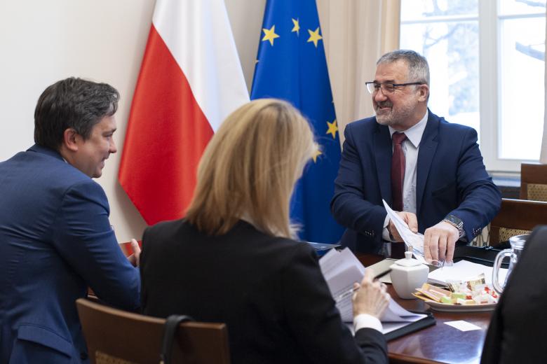 RPO Marcin Wiącek, Główny Geodeta Kraju Waldemar Izdebski oraz pracownicy BRPO rozmawiają przy konferencyjnym stole. W tle flagi Polski i Unii Europejskiej