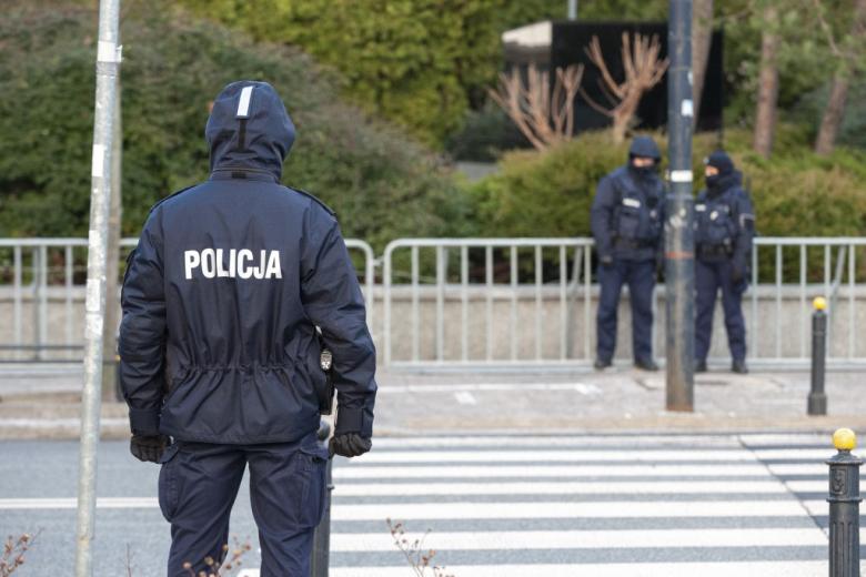 policjant na służbie stojący przy przejściu dla pieszych, po drugiej stronie ulicy kolejnych dwóch funkcjonariuszy