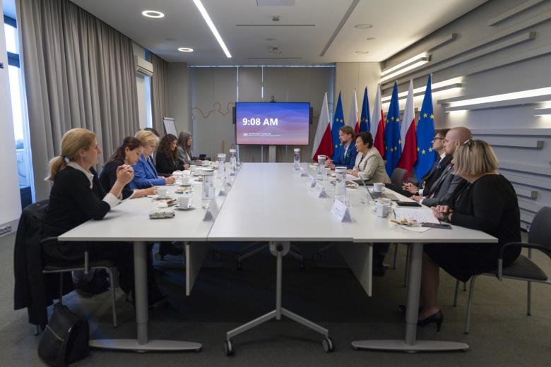 Grupa kilkunastu osób siedzących i rozmawiających przy stole konferencyjnym