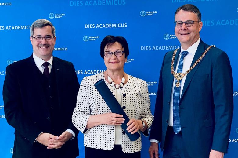 Dziekan Wydziału Prawa Uniwersytetu w Zurychu Thomas Gaechter, zastępczyni RPO Hanna Machińska oraz rektor Uniwersytetu w Zurychu Michael Schaepmann pozują na tle ścianki z logiem uniwersytetu. Hanna Machińska trzyma dyplom zapakowany w niebieską tubę.