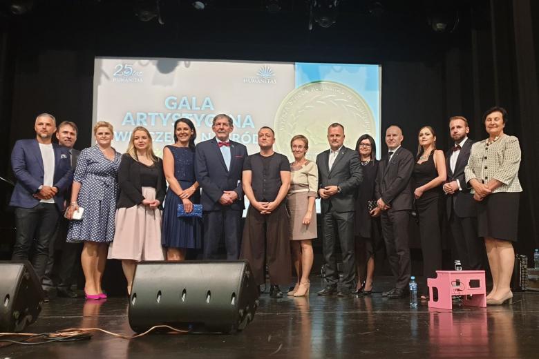 Kilkanaście osób pozuje do zdjęcia na scenie