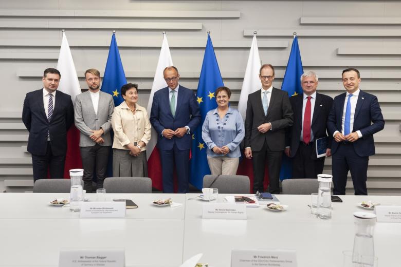 Dziewięć osób pozuje do zdjęcia na tle flag Polski i Unii Europejskiej