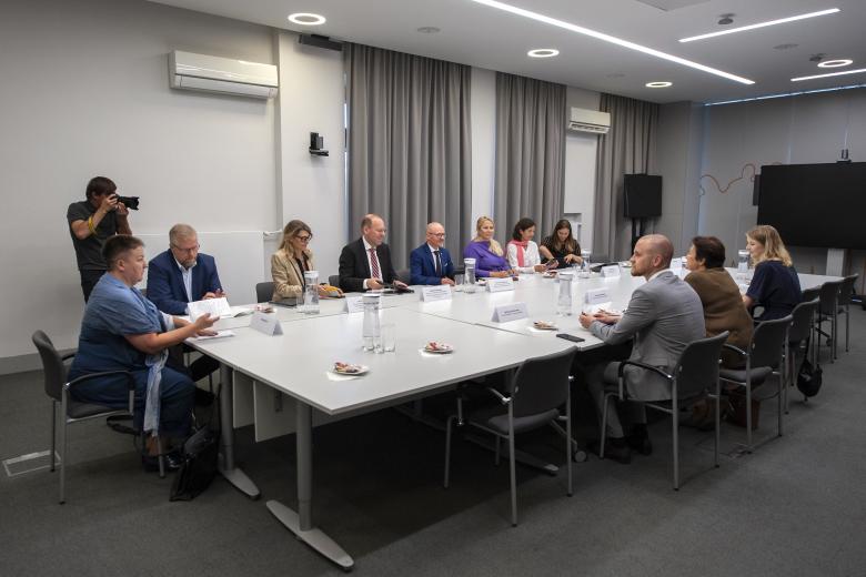 Członkowie delegacji oraz pracownicy biura RPO rozmawiający przy konferencyjnym stole. Na drugim planie stoi fotograf wykonujący zdjęcie.