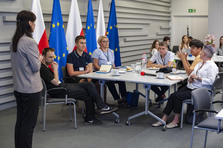 Prowadząca warsztat dyskutuje z uczestnikami warsztatu siedzącymi przy stole