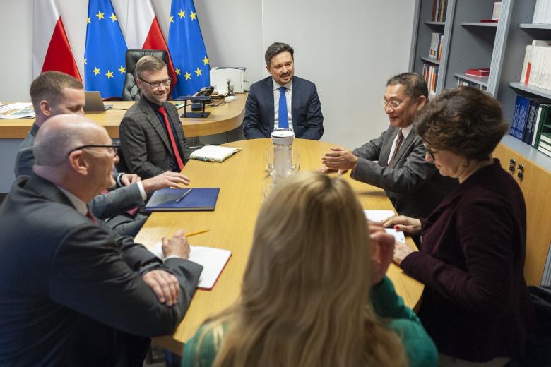 Grupa osób siedzących przy stole konferencyjnym i rozmawiających