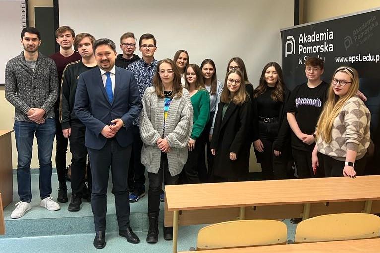 RPO Marcin Wiącek pozuje do zdjęcia z grupą studentów w sali wykładowej, w tle banner z napisem "Akademia Pomorska w Słupsku"