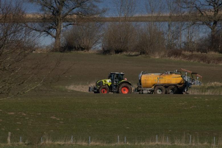 Ciągnik na polu rozrzuca nawóz z cysterny 