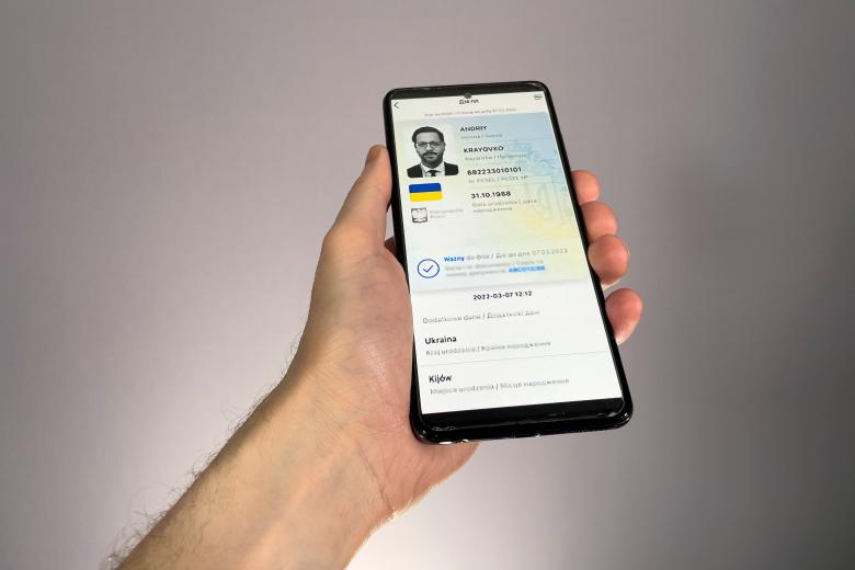 Dłoń trzymająca smartfon z otwartą aplikacją przedstawiającą dokument tożsamości