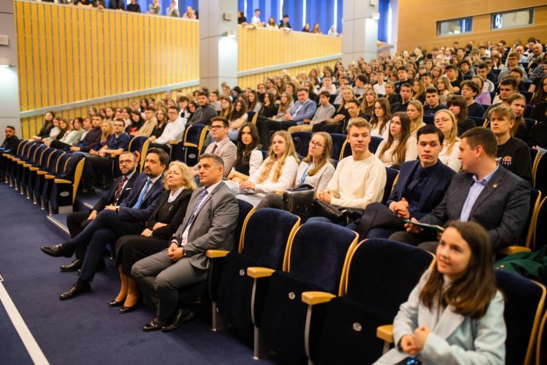 Kilkadziesiąt osób siedzi w rzędach na dużej auli wykładowej