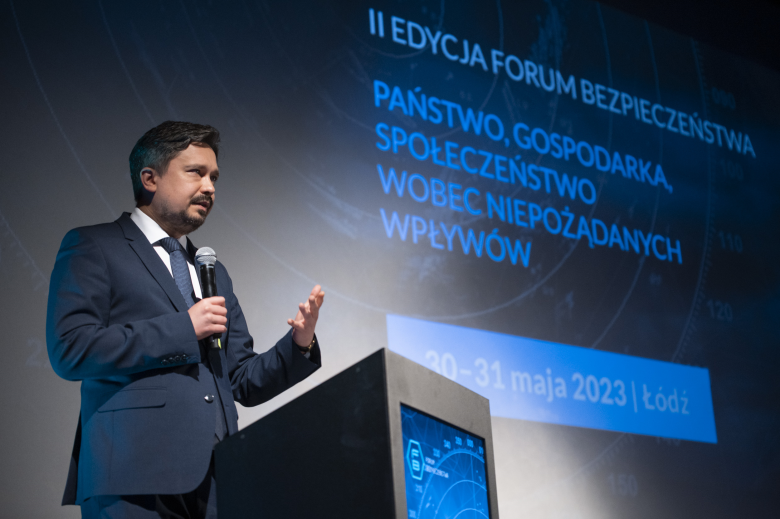 RPO Marcin Wiącek przemawia za mównicą na scenie, w tle duży telebim z napisem "II edycja Forum Bezpieczeństwa, Łódź 30-31 maja 2023 r."