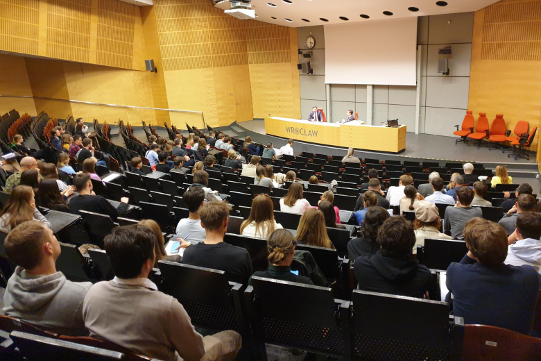 Duża aula wykładowa, w której siedzi kilkadziesiąt osób, na stole prezydialnym napis "WROCŁAW"