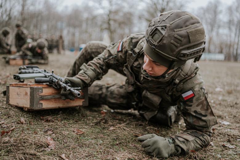 Żołnierz w mundurze polowym czołga się po błotnistym terenie poligonu