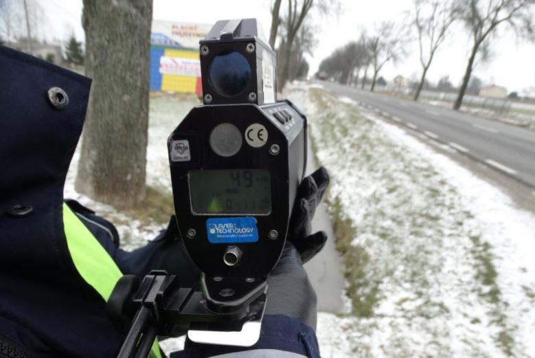 policjant trzyma ręczny radar prędkości  w kierunku drogi 