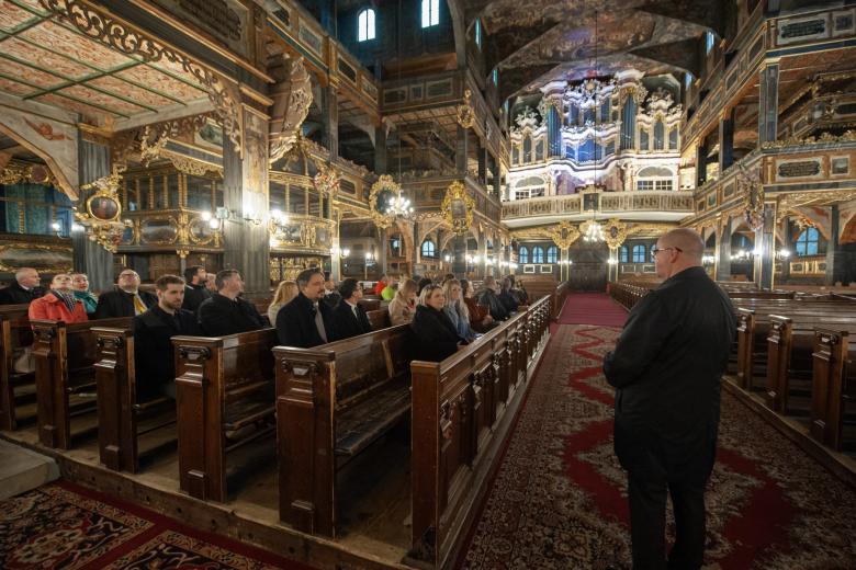 Kilkadziesiąt osób siedzi w ławach w zabytkowym, bogato zdobionym kościele