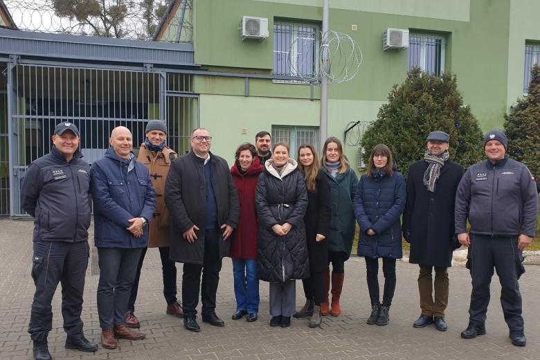 Grupa osób pozuje na stojąco do wspólnego zdjęcia na tle aresztu śledczego