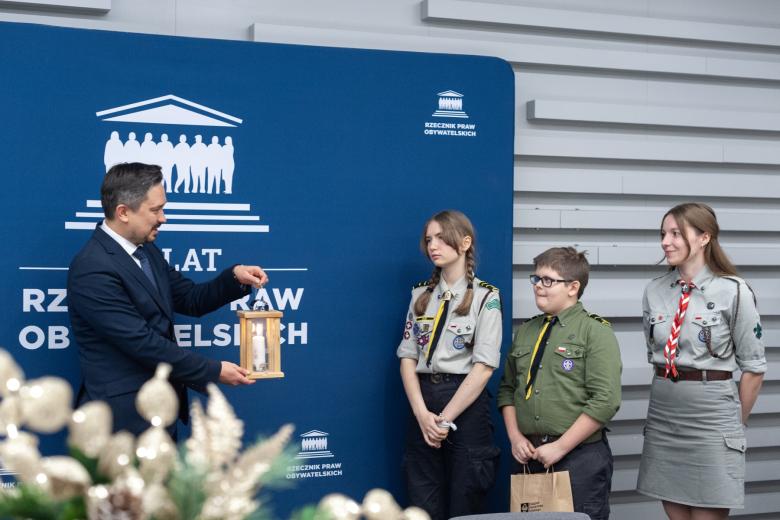 Troje harcerzy wręcza Marcinowi Wiąckowi zapaloną świecę