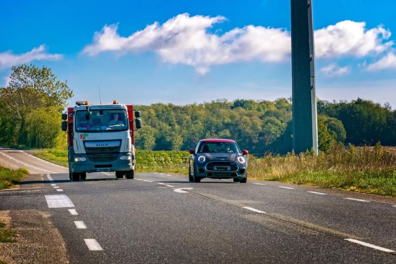 widziany z przodu samochód wyprzedza ciężarówkę na drodze w terenie niezabudowanym