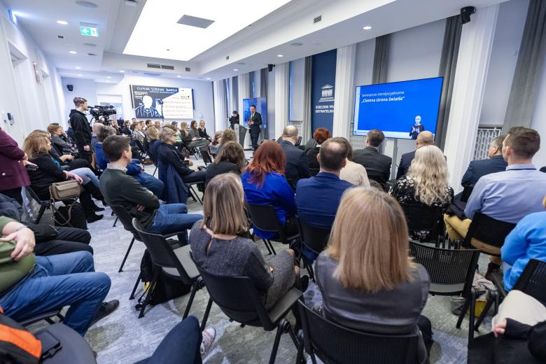 Kilkadziesiąt osób siedzących na sali konferencyjnej słucha wystąpienia osoby mówiącej za mównicą