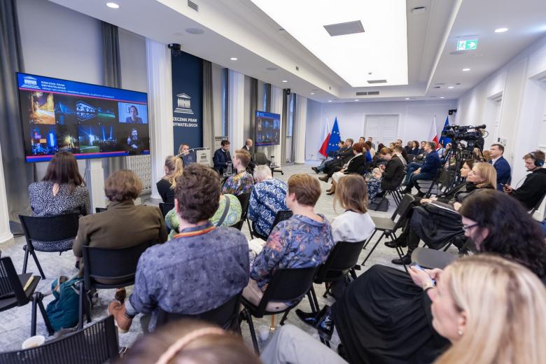 Kilkadziesiąt osób na sali konferencyjnej słucha wystąpienia prelegenta