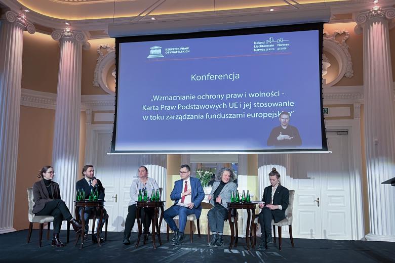 Sześcioro uczestników panelu siedzi na podium sali konferencyjnej i rozmawia.