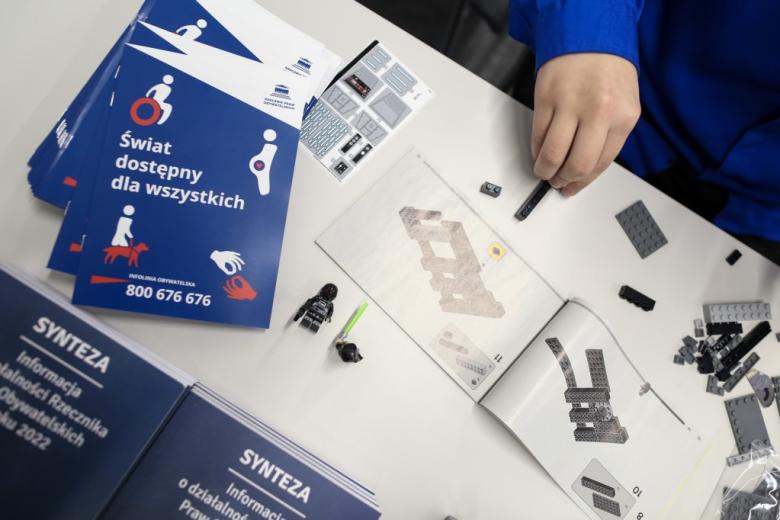 ręka osoby na stole, gdzie leżą klocki i wydawnictwa  