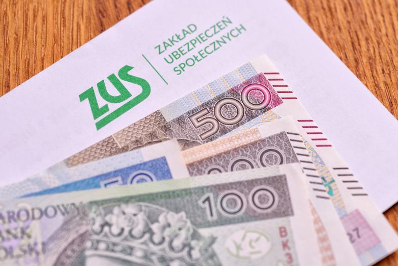 Plik banknotów ułożony na kopercie oznaczonej logiem Zakładu Ubezpieczeń Społecznych