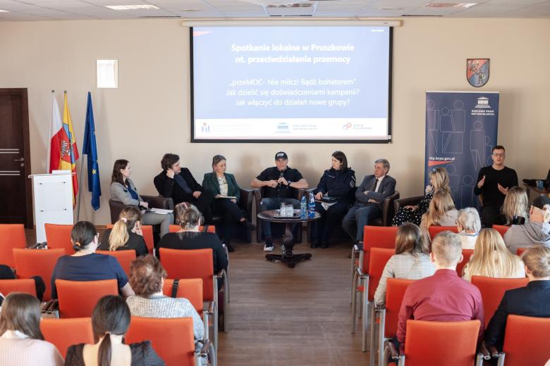 Sześć osób siedzących a fotelach przed widownią prowadzi rozmowę