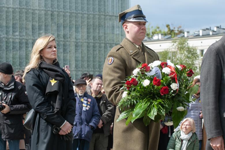 Dwie osoby stoją, jedna w mundurze wojskowym trzymająca bukiet białych i czerwonych róż