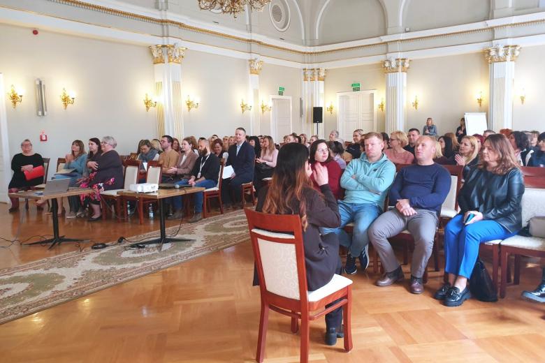 Kilkadziesiąt osób siedzących na dużej sali słucha wystąpienia