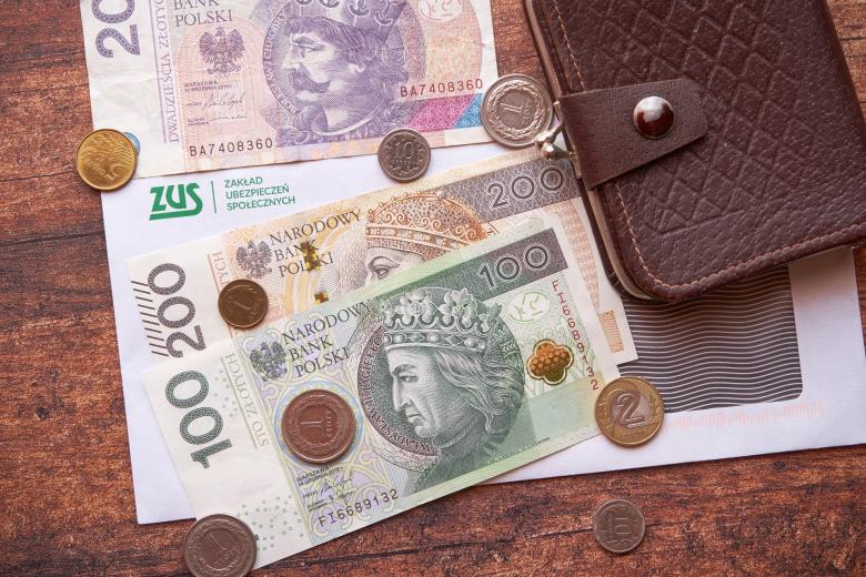 Portfel, banknoty i monety leżące na kopercie z nadrukowanym logiem Zakładu Ubezpieczeń Społecznych