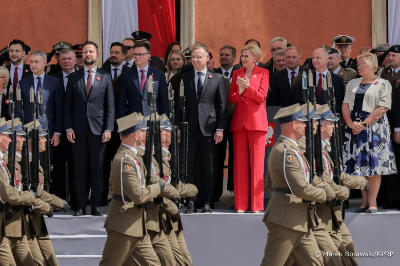 Uczestnicy obchodów, w tym RPO Marcin Wiącek, stoją obserwując defiladę żołnierzy w paradnych mundurach