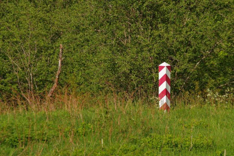 Słup w biało czerwone pasy stojący pośród traw i krzewów