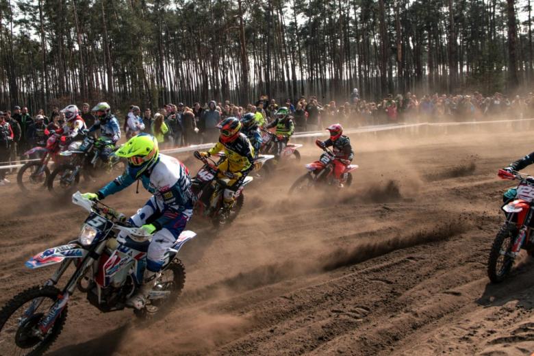 ścigające się motocrossy w terenie piaszczystym z widzami w tle 