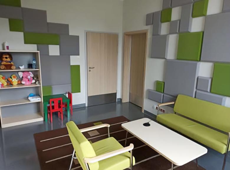 nowocześnie wyposażony pokój z zieloną kanapą i krzesłem przy drewnianej, niskiej ławie, dywanem, regałem z pluszowymi przytulankami i dziecięcym stoliczkiem i krzesełkami