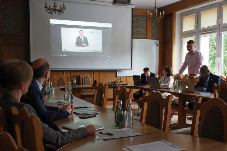Uczestnicy konferencji siedzą przy stole w kształcie podkowy i oglądają wystąpienie Rzecznika Praw Obywatelskich wyświetlane na ekranie