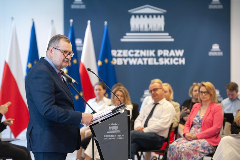 Krzysztof Olkowicz wygłasza laudację z mównicy. W tle siedzą słuchający go uczestnicy uroczystości.