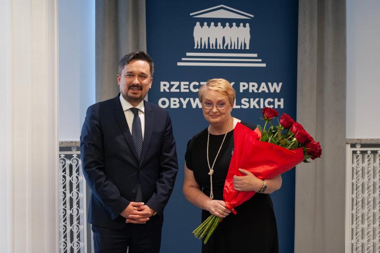 RPO Marcin Wiącek i Izabela Ciuńczyk pozują do zdjęcia, uśmiechając się. Izabela Ciuńczyk trzyma w rękach duży bukiet czerwonych róż.