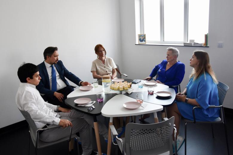 Pięć osób siedzi przy okrągłym stole i rozmawia