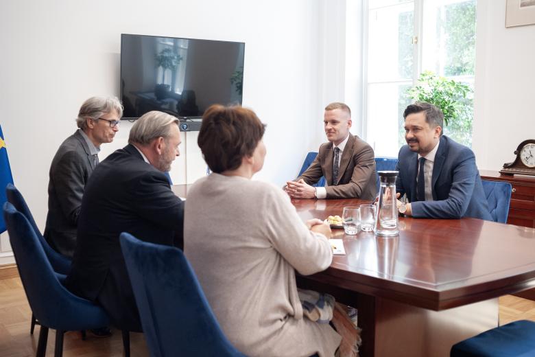 Pięć osób rozmawia siedząc przy stole konferencyjnym