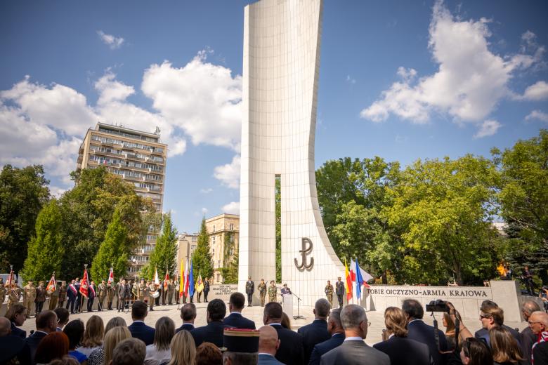 Ludzie zgromadzeni przed pomnikiem, przy którym odbywa się uroczystość złożenia wieńców